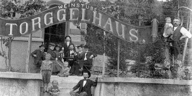 Eine Weingesellschaft mit Kind und Kegel posiert dem Fotographen vor dem neuerbauten Torggelhaus, dem heutigen Gasthaus Zeigerle.